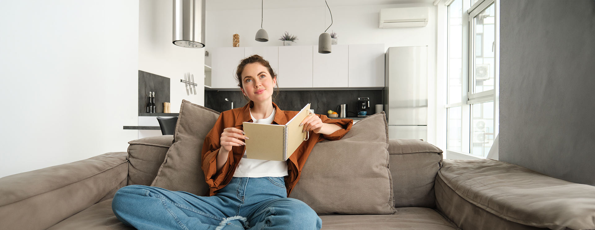 Portrait of young smiling beautiful woman, sitting on sofa in her living room, holding study material, doing homework, reading notes in notebook.